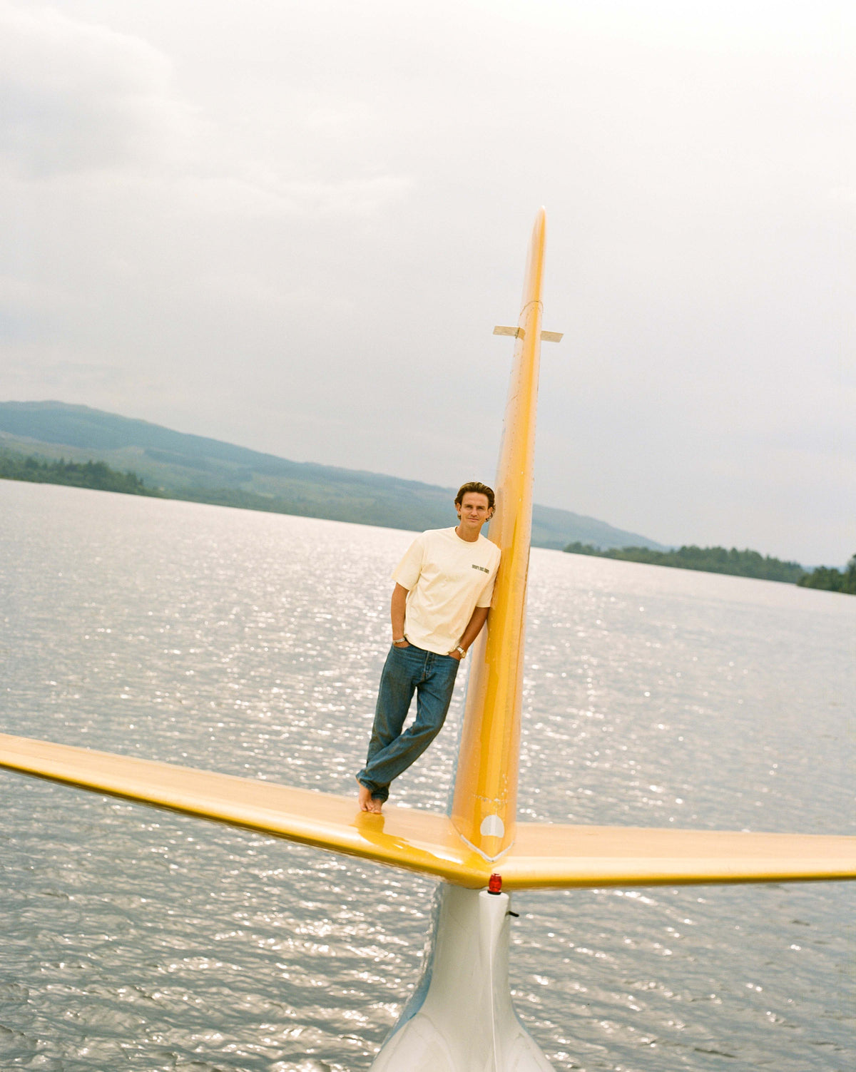 A man in a cream tee standing on the yellow tail over the lake