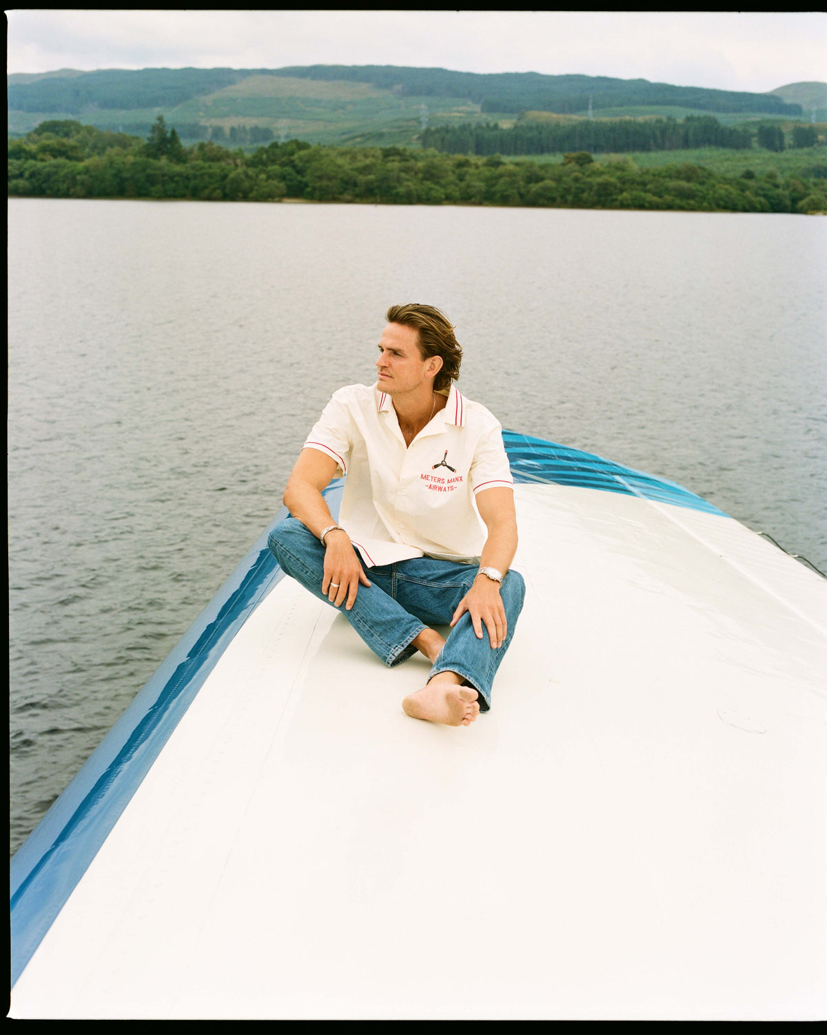 A man in a white shirt sitting on top of the hull on the lake