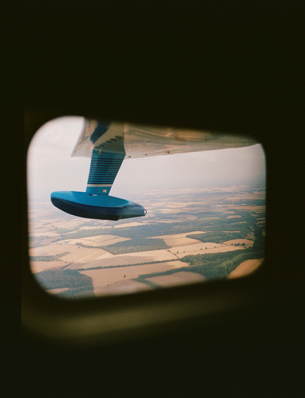 The wing float through a cabin window above farmland