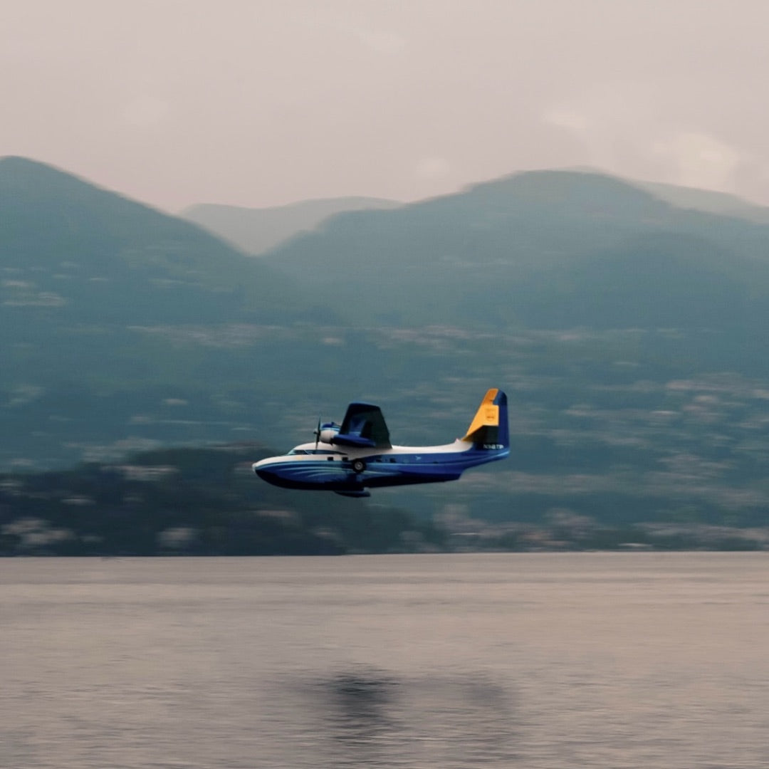 The Albatross flying low over a lake below mountains